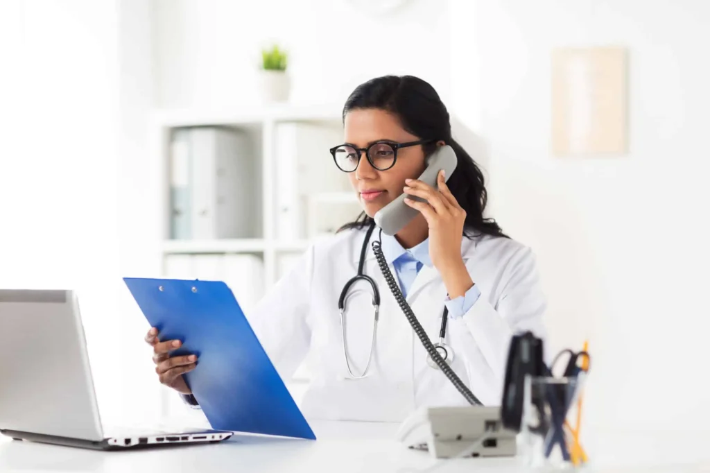 medicine, people and healthcare concept - happy female doctor with clipboard and laptop computer calling on phone at hospital